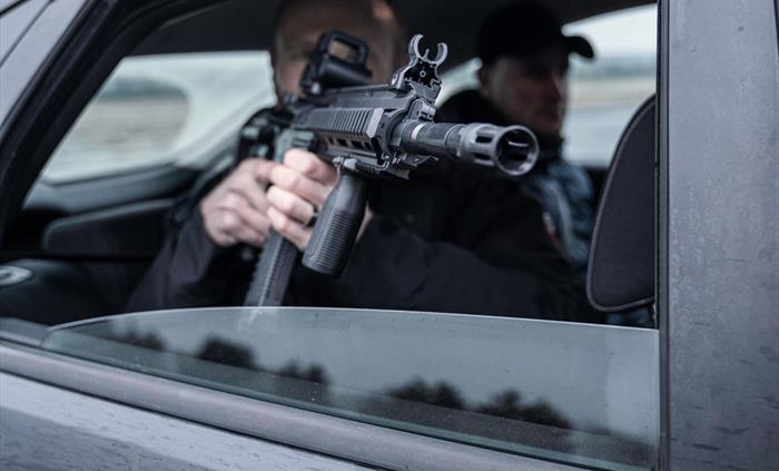 Man holding rifle from the rear of a vehicle